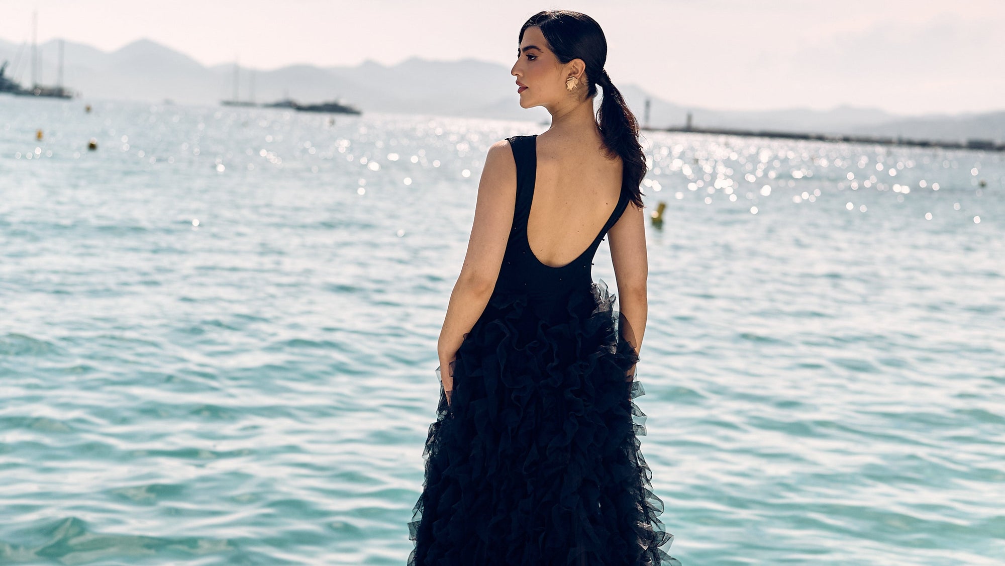 Woman in a black evening gown standing by a waterfront